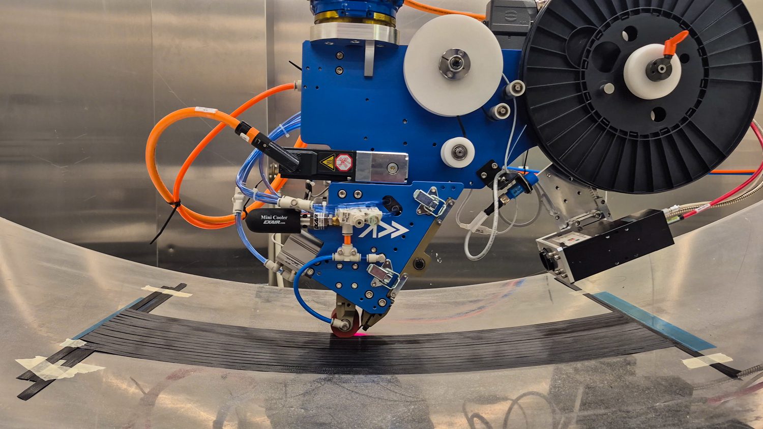 Addcomposites' AFP-XS placing carbon fiber tow under controlled compaction and heat on a curved tool — programmable, repeatable placement for load-critical carbon components.