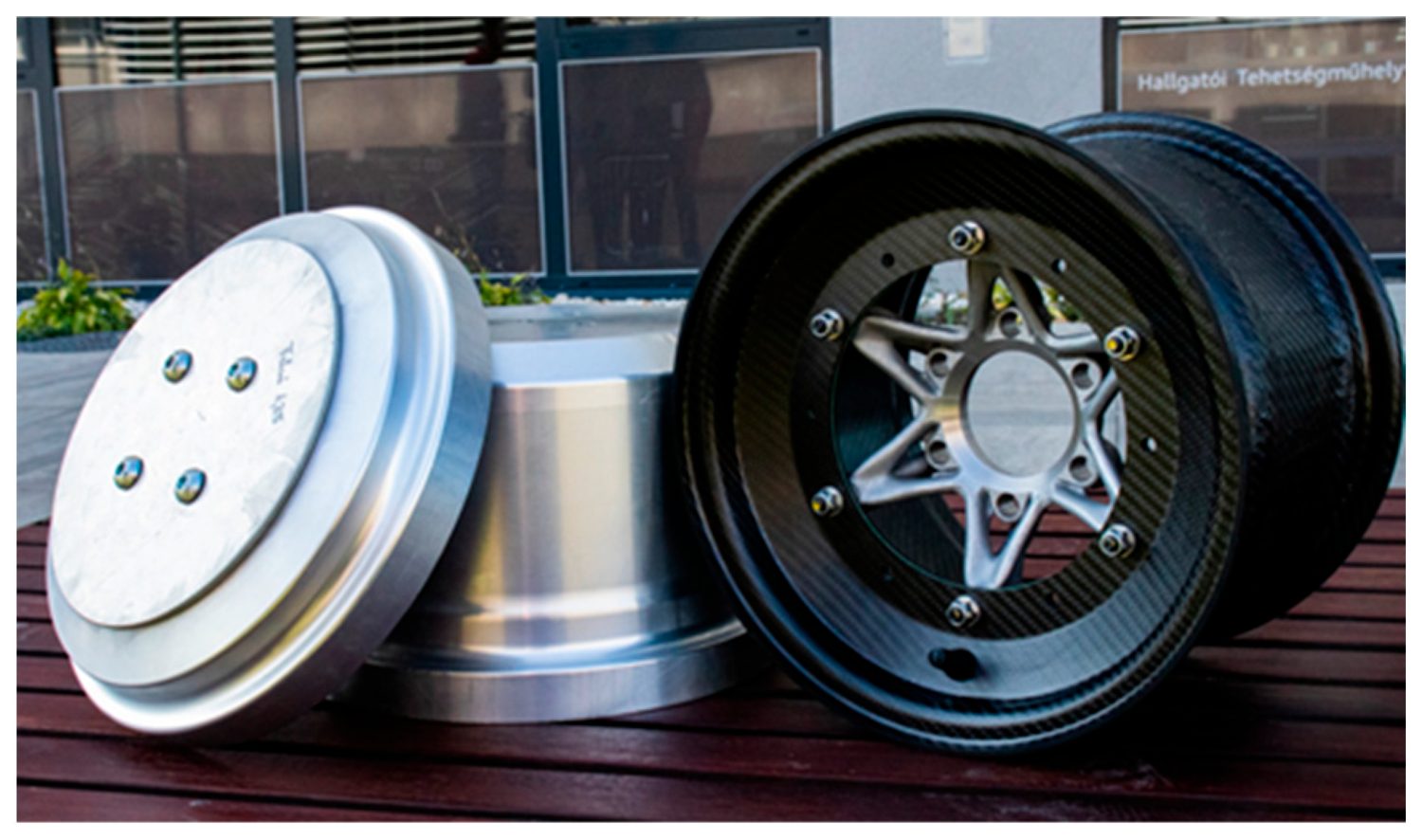 A silver aluminum disc-shaped laminating tool beside a finished three-piece CFRP rim with a star-spoked 3D-printed center and glossy woven-carbon barrel.