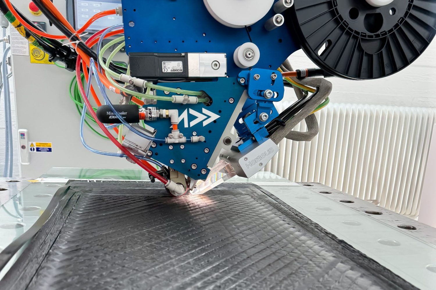 An Addcomposites AFP-XS toolhead places, orients, and consolidates carbon-fiber tow onto a laminate in a single pass.