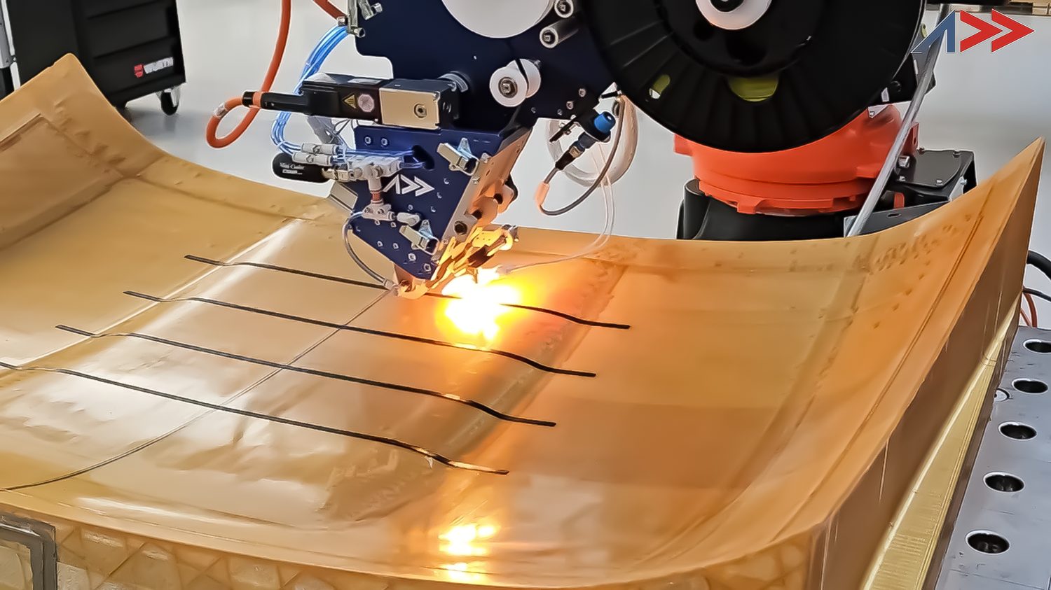 The Addcomposites AFP-XS head depositing carbon-fibre tow onto a curved tool — repeatable, heat-assisted machine placement in place of manual cutting and hand lay-up.
