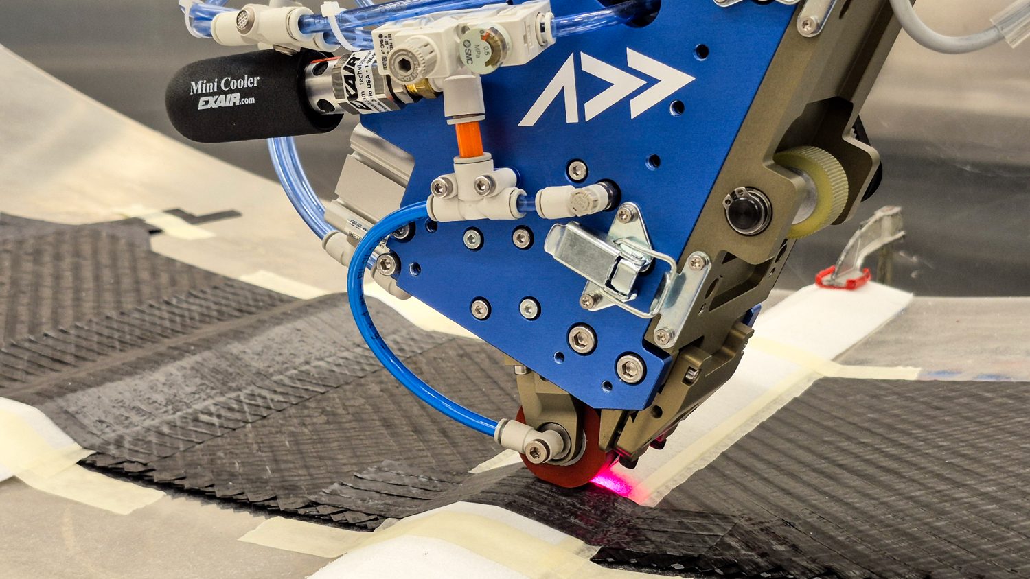 An Addcomposites AFP-XS head placing carbon fibre onto a curved tool, with the compaction roller in contact.