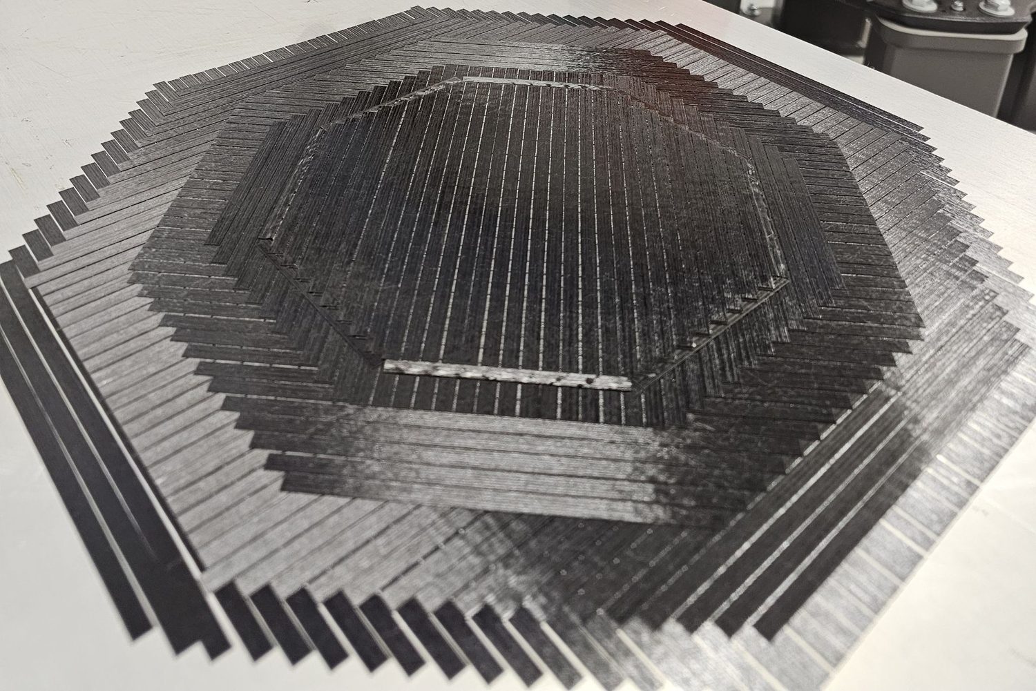 Carbon-fiber plies laid up at alternating angles — the stepped courses show how fiber direction is placed and sequenced layer by layer.